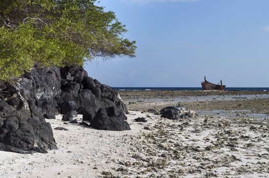 Volcanic rock in low tide shoreline with aground boat