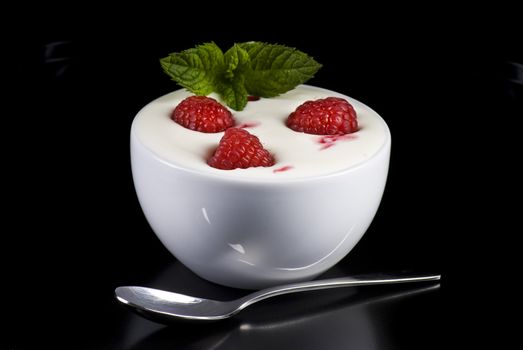 Bowl of yogurt with raspberries and mint on black background