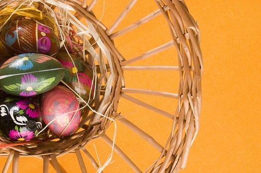 willow basket with colorful easter eggs over orange background