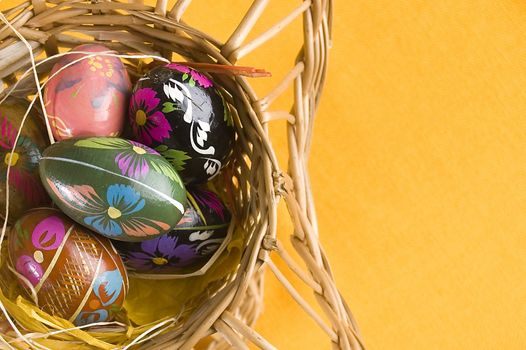 willow basket with colorful easter eggs over orange background