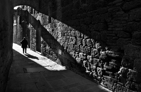 A pedestrian in a narrow medieval street in San Gimignano, Tuscany, Italy