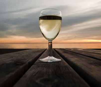 A glass of white wine on a beach at sunset