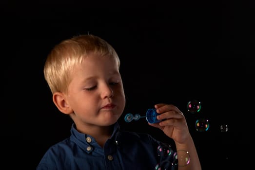 Blond boy having fun blowing colorful soap bubbles