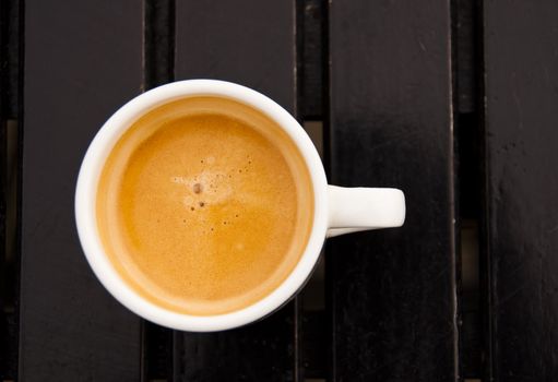 An espresso in a white cup on a dark wood table