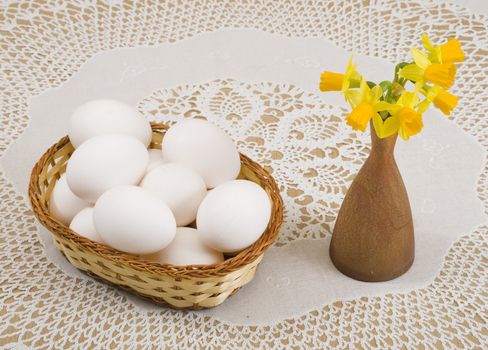 a basket of eggs and yellow daffodils in a vase