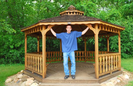 A young man standing in a wooden gazebo.