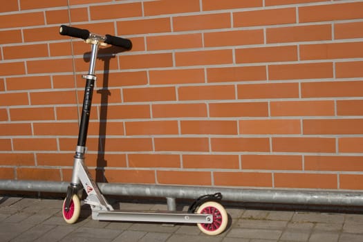 A push-scooter in front of a red bricked wall.