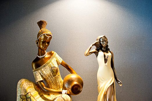 Two figurines of the woman, one African with a jug, other white.
