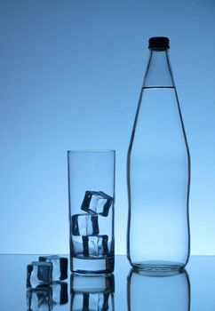 Water bottle, glass and ice on blue background