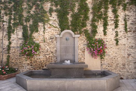 Urban fountain and flowers onext to a brickwall