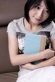 Thinking beautiful girl with the book sitting on sofa