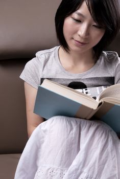 Portrait of a young woman sitting on sofa reading book