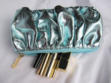 A shiny turquoise cosmetics bag with a few make up products.