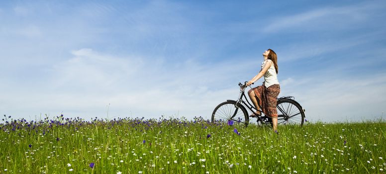 Happy young woman with a vintage bicycle on a green meadow