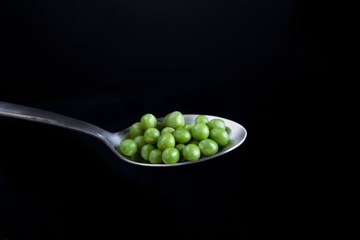 Fresh green peas on spoon with black background.