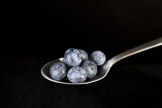 Fresh blueberries on spoon with black background.