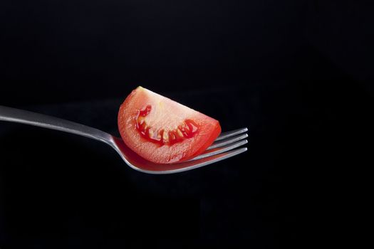 Fresh tomato wedge on fork with black background