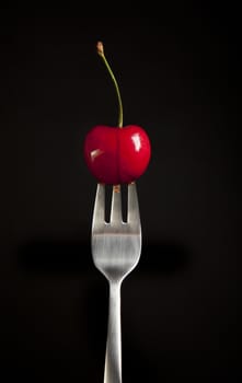 Fresh cherry on fork with black background