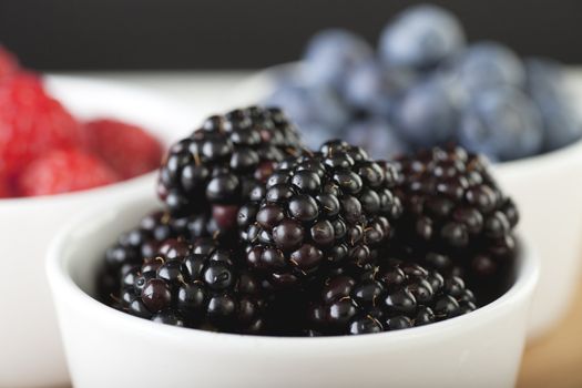 White bowl of blackberries with blueberries and raspberries in background