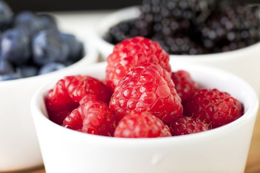 Bowl of fresh raspberries with blueberries and blackberries in background.
