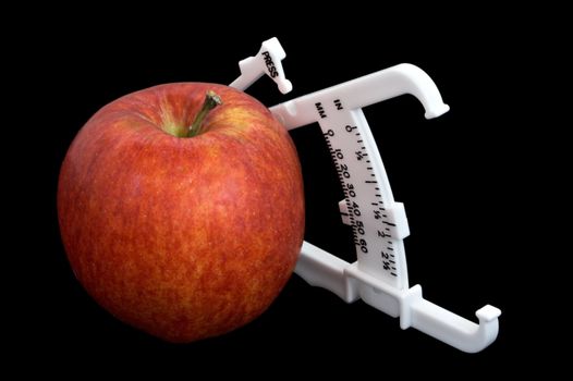 An apple and bodyfat calipers isolated over a black background
