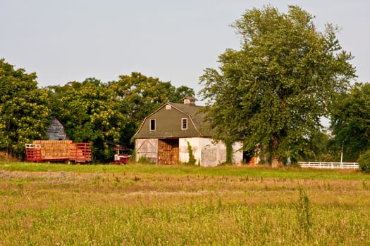 A barn in the country with a trailer full of hay. Photo was captured in late evening sunlight.