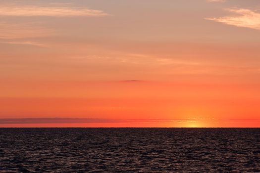 A morning sunrise over water. Photo was taken just prior to the sun coming over the horizon. The sky is vibrant orange and yellow.