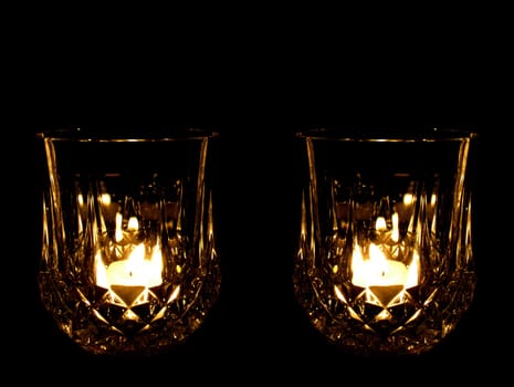 A lead crystal whisky glass illuminated by a tealight candle, against a black background