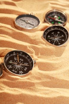 Conceptual background with few compasses lying on sand. Vertical image