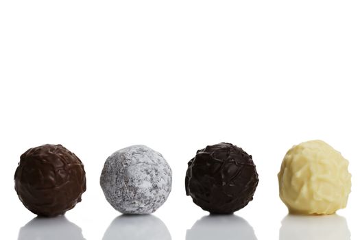 four different truffle pralines in a row on white background