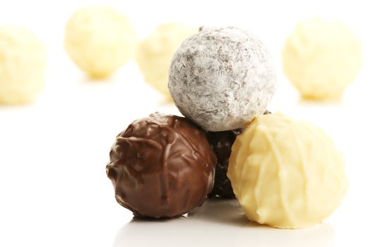 stack of different truffle pralines in front of yellow truffles on white background