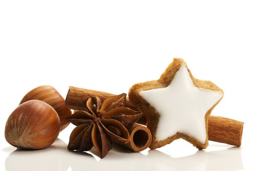 star shaped cinnamon biscuit with cinnamon sticks and hazelnuts on white background