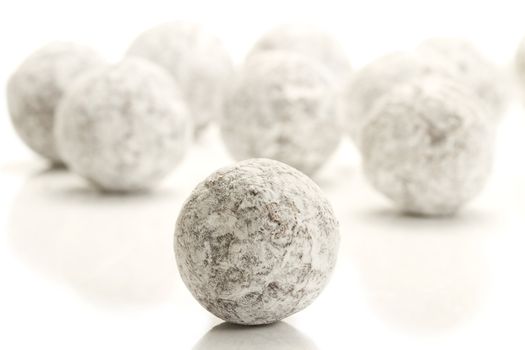 sugar powder covered truffle praline in front of many on white background