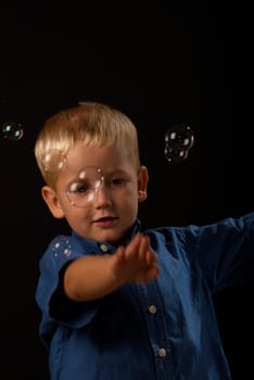 Little blond boy trying to catch flying soap bubbles