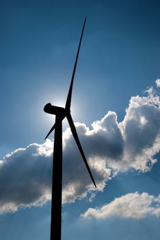 Wind turbine in the back light of the sun with blue sky and clouds.