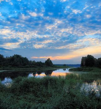 over sunset clouds illuminate blue sky over evening lake