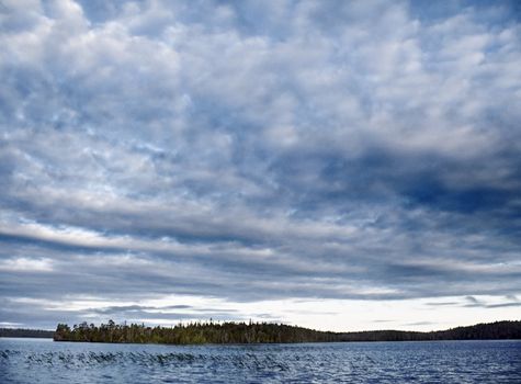 The evening sun through clouds shines cold waters of northern lake