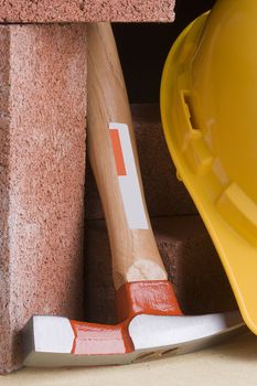 Stonemason's hammer next to red bricks and a yellow hard hat.