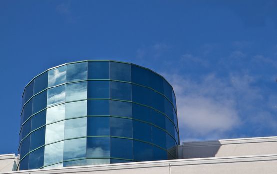 Angled reflective windowed Cylinder Building reflecting blue sky and clouds