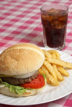 A freshly cooked hamburger and fries meal on a checkered tablecloth.