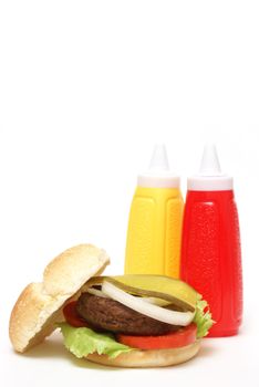 An isolated hamburger with mustard and ketchup bottles.