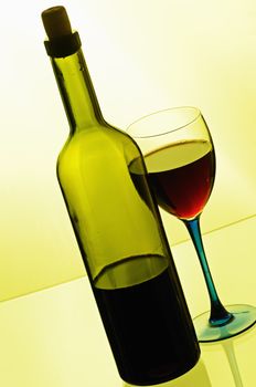 Bottle of red wine with glass on yellow background