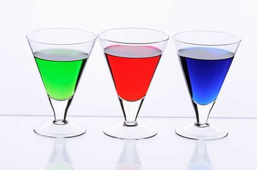 Three transparent glasses with multi-coloured drinks