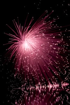 Vibrant red fibre optic strands cascading downwards and reflecting into the foreground. Black background.