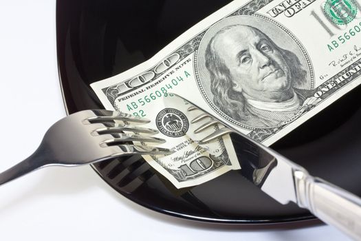 One hundred dollar banknote on a black plate with knife and fork