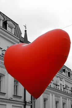 Big red heart ballon is hanging over old stree