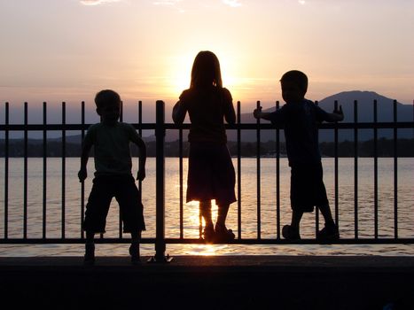 Children in silhouette on a fence by the lake