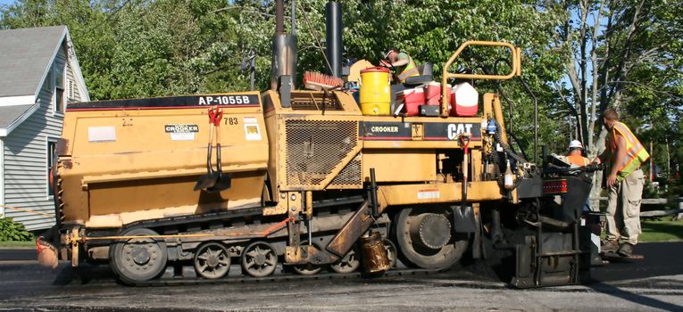 Part of a crew applying asphalt to a public roadway