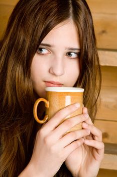 Portrait of the dark-haired girl with a mug close up  a wooden ladder background
