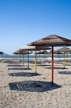 Set of beach umbrellas on sand making shadows under the blue clear sky in hot day
